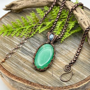 May include: A copper wire wrapped pendant necklace featuring a green oval gemstone and a smaller blue gemstone. The necklace has a copper chain with a lobster clasp.