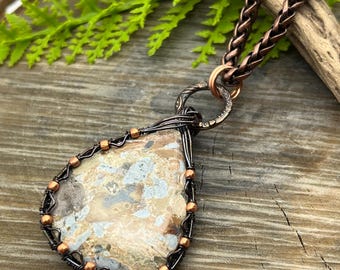 May include: A copper wire wrapped pendant featuring a teardrop-shaped, light brown, gray, and white agate stone with copper beads. The pendant is attached to a copper chain.