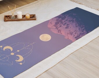 Pode incluir: Um tapete de ioga com um design celestial. O tapete apresenta um gradiente de roxo e azul com uma lua cheia e uma cordilheira em tons de rosa e roxo. Formas geométricas douradas na parte inferior.