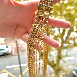 Może przedstawiać: Złoty naszyjnik z łańcuszka o wielu splotach i zapięciem na zatrzask. Naszyjnik jest trzymany w dłoni, a tło jest rozmyte.