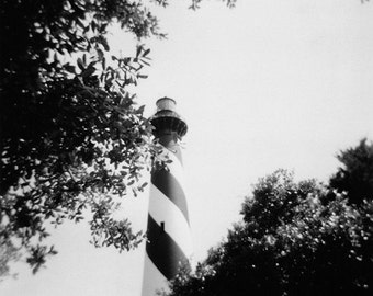 Puede incluir: Un faro de rayas blancas y negras se alza alto contra un cielo despejado. El faro está rodeado de árboles.