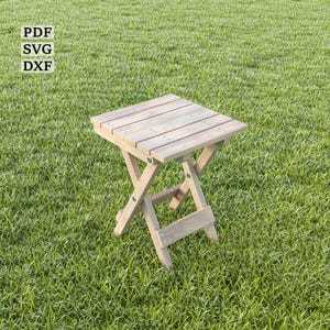 Op de afbeelding: Een houten opklapbare tafel met een natuurlijke afwerking. De tafel is gemaakt van houten latten en heeft een eenvoudig, rustiek ontwerp. Hij staat op een groen gazon.