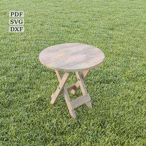 May include: A wooden folding table with a round top and a natural wood finish. The table is sitting on a green grassy lawn.