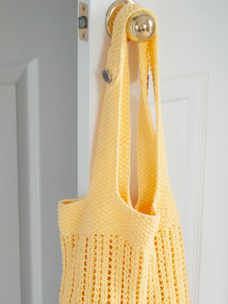 May include: A yellow crocheted tote bag hanging on a white door handle. The bag has a simple, open weave design.