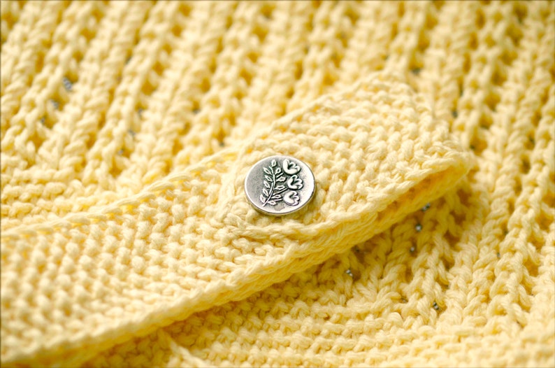 May include: A close-up of a yellow crocheted fabric with a silver button featuring a floral design.