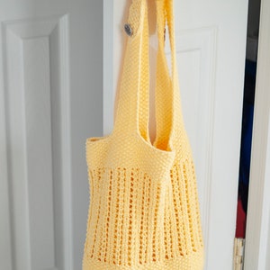 May include: A yellow crocheted tote bag with a woven design hangs on a white door handle.