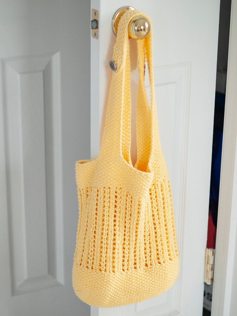 May include: A yellow crocheted tote bag with a woven design hangs on a white door handle.