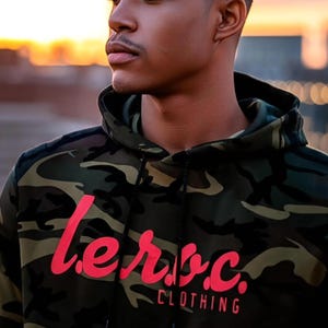 Hoodie met camouflageprint en fluorescerende oranje tekst | l.e.o.c. Kleding Stoere streetwear | Uniseks camouflagetrui | Grafische hoodie in outdoorstijl