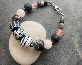May include: A bracelet with black, white, and pink beads. The beads are made of lava rock, agate, and rose quartz. The bracelet has a silver clasp.
