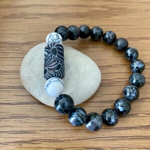 Peut inclure: Un bracelet de perles à motifs noir et blanc avec une perle cylindrique à motifs noir et blanc. Le bracelet est composé de perles rondes tachetées de noir et de blanc.