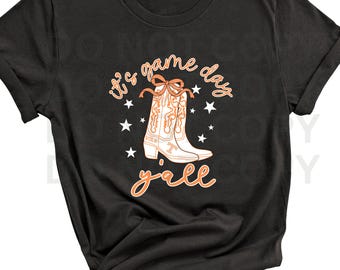Puede incluir: Camiseta negra con un gráfico de bota de vaquero, estrellas y el texto "it's game day y'all" en naranja. La bota tiene detalles en naranja y la palabra "VOLS" es visible.