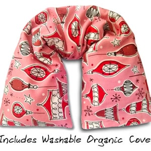 May include: Pink fabric neck pillow with a Christmas ornament pattern. The pillow is shaped like a U and has a white background with red and black ornaments. The text "Includes Washable Organic Cover" is printed below the pillow.