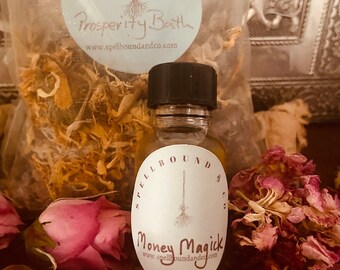 May include: A small glass bottle with a black cap and a label that reads "Money Magick" sits among dried flowers and petals. A bag labeled "Prosperity Bath" is visible in the background. The products are from Spellbound & Co.