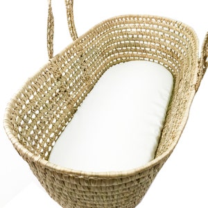 May include: A woven wicker bassinet with a white mattress. The bassinet has two handles on the sides.