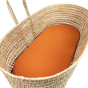 May include: A woven wicker bassinet with a handle and an orange fitted sheet.