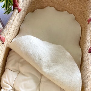 May include: A woven wicker basket with a white cotton liner and a white cotton mattress pad. The basket is lined with a white cotton fabric and has a white cotton mattress pad inside.