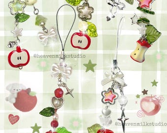 May include: A collection of decorative phone charms featuring red apple, star, and bow designs. Charms include white bows, green leaves, and various beads. The background is a light green plaid pattern with star and heart accents.
