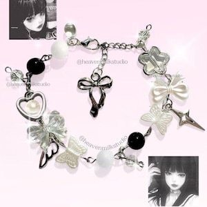 May include: A silver-toned charm bracelet featuring black and white beads, clear butterfly charms, a heart charm with a pearl center, a bow charm, and a star-shaped charm. The bracelet includes a lobster clasp and the text @heavenmilkstudio.