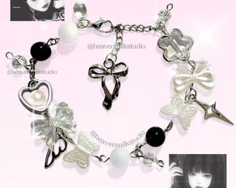 May include: A silver-toned charm bracelet featuring black and white beads, clear butterfly charms, a heart charm with a pearl center, a bow charm, and a star-shaped charm. The bracelet includes a lobster clasp and the text @heavenmilkstudio.