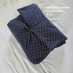 Pode incluir: Uma bolsa de cosméticos azul marinho com bolinhas brancas, amarrada com um cordão a condizer. A bolsa está dobrada e parece ser feita de tecido. O texto na imagem diz "PDF SEWING PATTERN COSMETIC BAG".