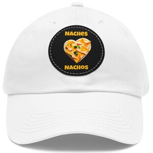 May include: White baseball cap with a black and white circular patch featuring a heart-shaped image of nachos with cheese and green onions. The patch has the text "NACHES" above the image and "NACHOS" below the image.