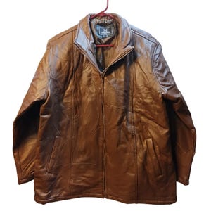 May include: A brown leather jacket with a full zipper closure and two front pockets. The jacket is hanging on a red hanger. The leather has a patchwork design.