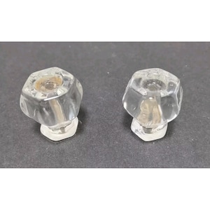 May include: Two clear, faceted glass cabinet knobs. Each knob has a hexagonal base and a rounded, octagonal top. The knobs are transparent, allowing light to pass through, and are set against a dark background.