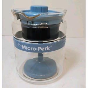 May include: A clear glass coffee maker with blue plastic components. The Micro-Perk brand name is printed on the side. The coffee maker has a blue lid and a blue base. The filter basket is visible inside the glass carafe.