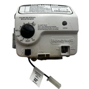 May include: A white Honeywell gas control valve with a black control knob and a status light. The valve has text that reads "Scalding Risk Increases With Hotter Water" and "To Light Pilot". A tag with text is attached.