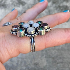 May include: A silver ring with a flower-shaped design featuring white moonstone and purple amethyst gemstones.