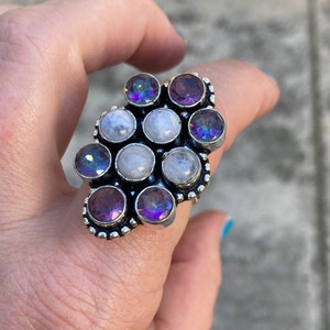 May include: A silver ring with a cluster of white moonstone and purple amethyst gemstones. The ring has a beaded design around the stones.