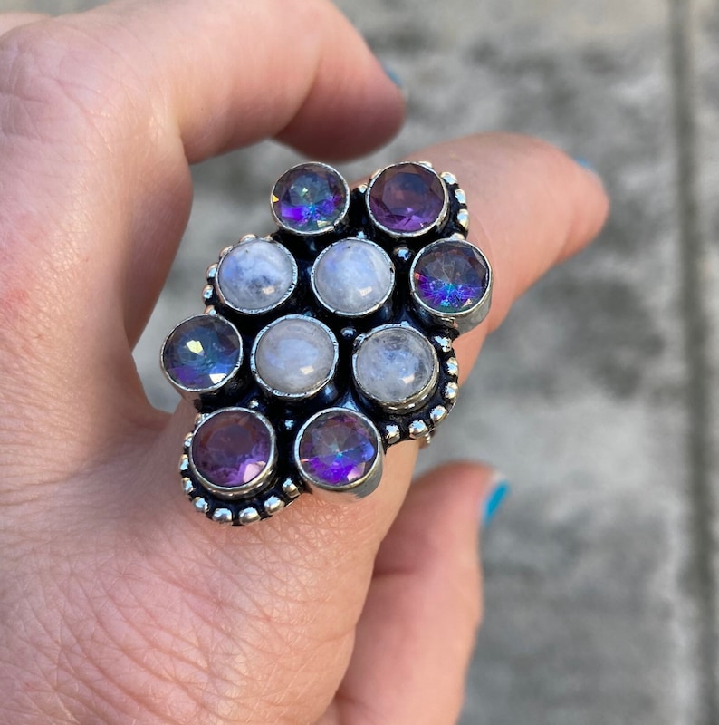 May include: A silver ring with a cluster of white moonstone and purple amethyst gemstones. The ring has a beaded design around the stones.