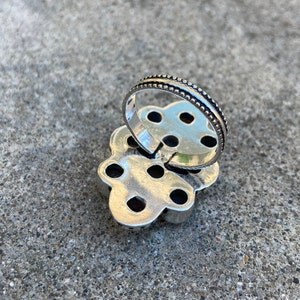 May include: Silver ring with a flower design and multiple small stones. The ring is open on the back and has a beaded edge.