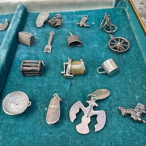 May include: A collection of silver charm bracelets, displayed in a velvet-lined box. The charms include a boot, a bell, a wheel, a shoe, a bird, a house, a compass, and a variety of other designs.
