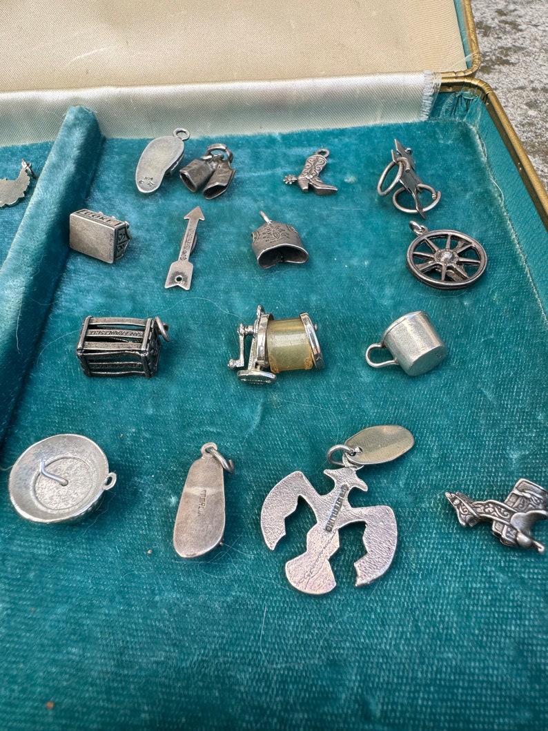 May include: A collection of silver charm bracelets, displayed in a velvet-lined box. The charms include a boot, a bell, a wheel, a shoe, a bird, a house, a compass, and a variety of other designs.