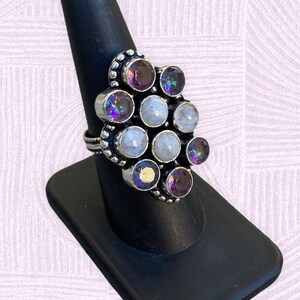 May include: A silver ring with a cluster of round, iridescent gemstones. The ring features a mix of white and purple stones, set in a silver band.