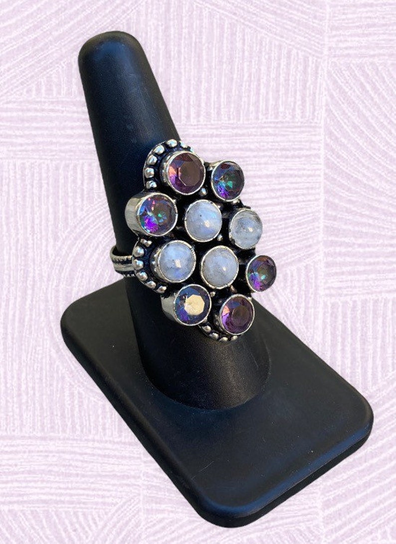 May include: A silver ring with a cluster of round, iridescent gemstones. The ring features a mix of white and purple stones, set in a silver band.