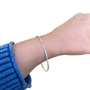 May include: A silver hammered bangle bracelet on a person's wrist.