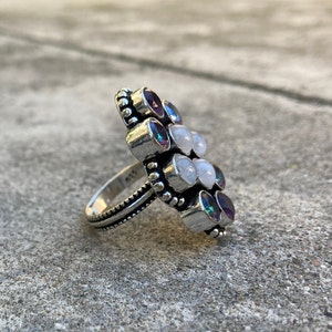 May include: A silver ring with a cluster of white and purple gemstones. The ring has a beaded band and the stones are set in a flower-like design.