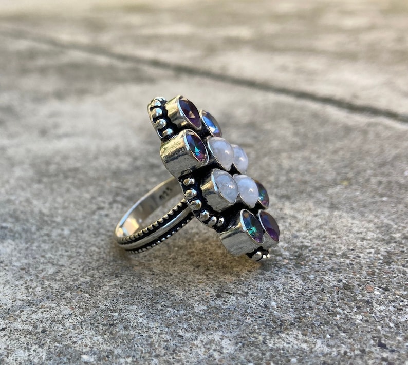 May include: A silver ring with a cluster of white and purple gemstones. The ring has a beaded band and the stones are set in a flower-like design.