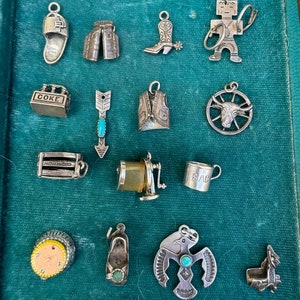 May include: A collection of 14 silver charm pendants, including a cowboy boot, a vest, a Native American headdress, a Coke bottle, a baby cup, a pair of cowboy chaps, a pair of slippers, a Hollywood sign, a wheel with a bull's head, an arrow with a turquoise stone, a Native American figure, and a pair of slippers.