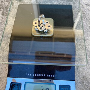 May include: A silver ring with a floral design and purple stones, weighing 10 grams on a digital scale.