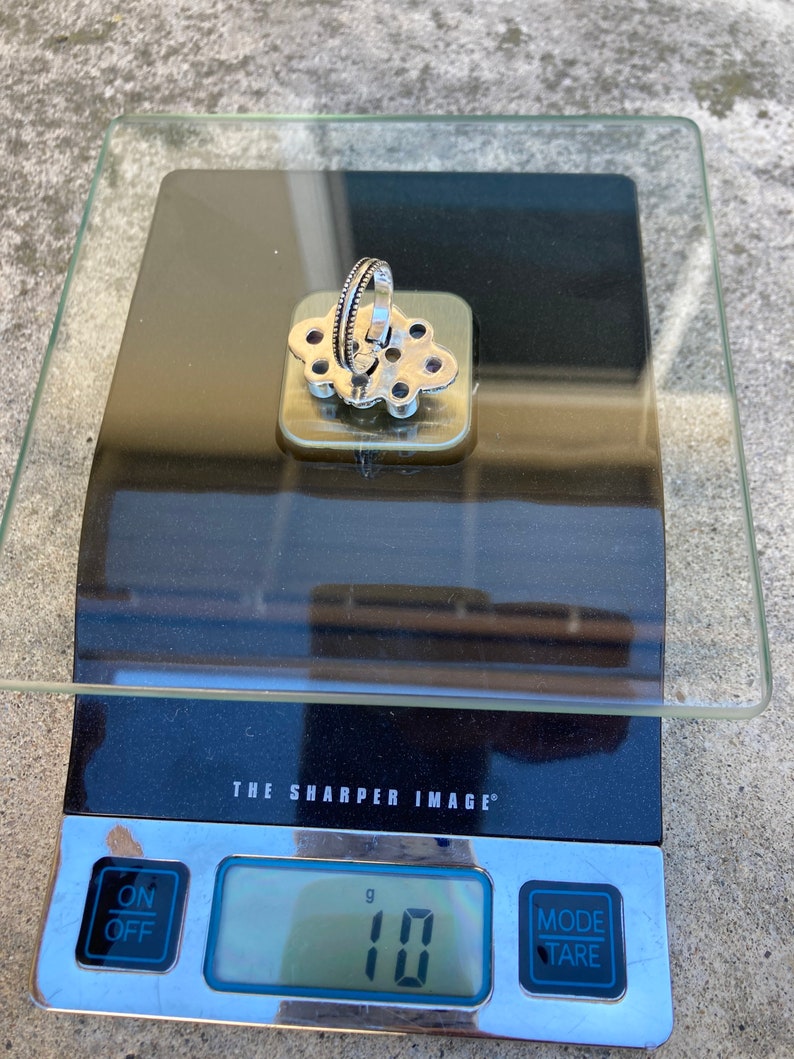 May include: A silver ring with a floral design and purple stones, weighing 10 grams on a digital scale.