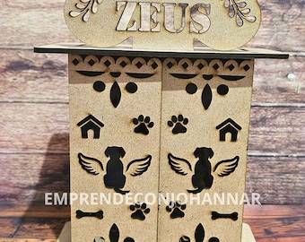 May include: A wooden pet memorial box with the name "ZEUS" cut out on a bone-shaped top. The box features cut-out paw prints, dog silhouettes with wings, and the text "EMPRENDECONIOHANNAR". The box is made of light brown wood.