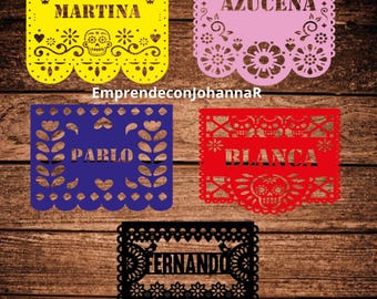 May include: Four colorful paper banners with cut-out designs, featuring the names "Martina", "Azucena", "Pablo", and "Blanca". The banners are decorated with traditional Mexican Day of the Dead imagery, including skulls, flowers, and hearts.