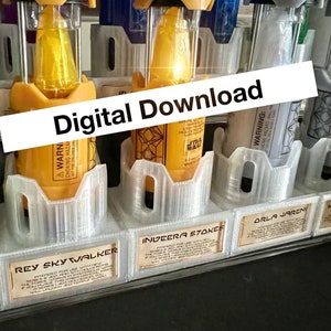 以下が含まれることがあります： 黄色、オレンジ、白の液体が入った透明なプラスチック容器6個セット。各容器には、レイ・スカイウォーカー、インベラ・ストークス、オーラ・ジャレンなど、スター・ウォーズ・フランチャイズのキャラクター名が書かれたラベルが付いています。容器は白い棚に一列に並んでいます。画像には「デジタルダウンロード」というテキストが重ねられています。