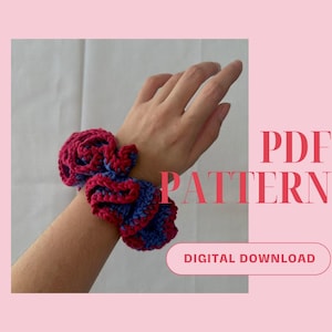 May include: A crochet hair scrunchie in shades of red and blue. The scrunchie is made with a ruffled design and is shown on a person's wrist. The image includes the text "PDF PATTERN DIGITAL DOWNLOAD".