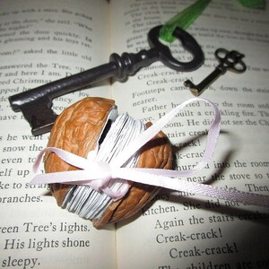 May include: A vintage-style key with a brown wooden handle and a metal bow, a walnut shell with a pink ribbon, and a book with text about a Christmas tree.