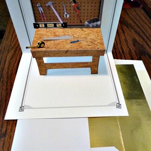 May include: A pop-up card featuring a workbench with tools, a tape measure, and a saw. The card is decorated with a gold border and the text "www.PetrinaCaseStudio.ETSY.com NO. 954".