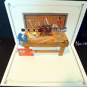 May include: A pop-up card depicting a wooden workbench with various tools, including a hammer, saw, wrench, level, and nails. The card is decorated with a gray and brown pegboard and a red toolbox. The card is labeled "No. 1901".